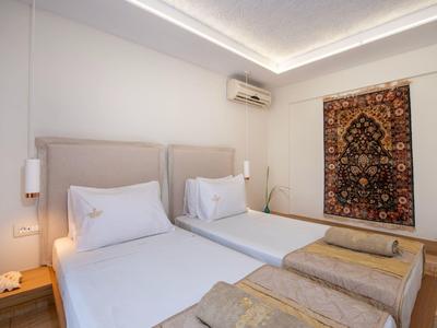 Nowoczesny pokój hotelowy z dwoma pojedynczymi łóżkami, dywanem na ścianie i pośrednim oświetleniem sufitowym.