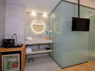 Nowoczesny pokój hotelowy z okrągłym podświetlanym lustrem i szklaną łazienką.