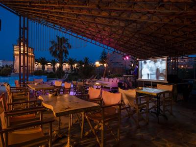 Zadaszony taras na zewnątrz z stołami i krzesłami o zmierzchu, widoczny ekran do projekcji