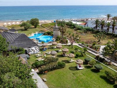 Ogród hotelowy z basenem, parasolami, trawnikami i widokiem na morze i plażę.