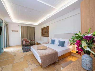 Nowoczesny pokój hotelowy z dużym łóżkiem, oświetleniem sufitowym LED i częścią wypoczynkową z fotelami.