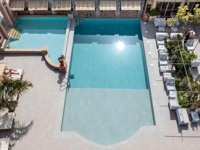 Basen hotelowy z leżakami i zielonymi roślinami w słoneczny dzień.