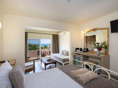 Jasny pokój hotelowy z podwójnym łóżkiem, miejscem do siedzenia, balkonem i widokiem na morze.