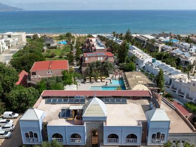 Kompleks hotelowy z basenem otoczony białymi budynkami i morzem w tle