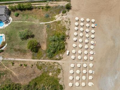 Widok z lotu ptaka na hotel z basenem, leżakami i parasolami na plaży.