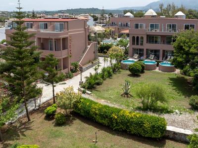 Kompleks hotelowy z kilkoma budynkami, zielonymi ogrodami i małym basenem przy słonecznej pogodzie