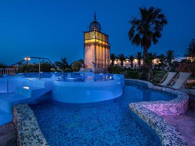 Oświetlony basen na zewnątrz z leżakami i palmami o zmierzchu.