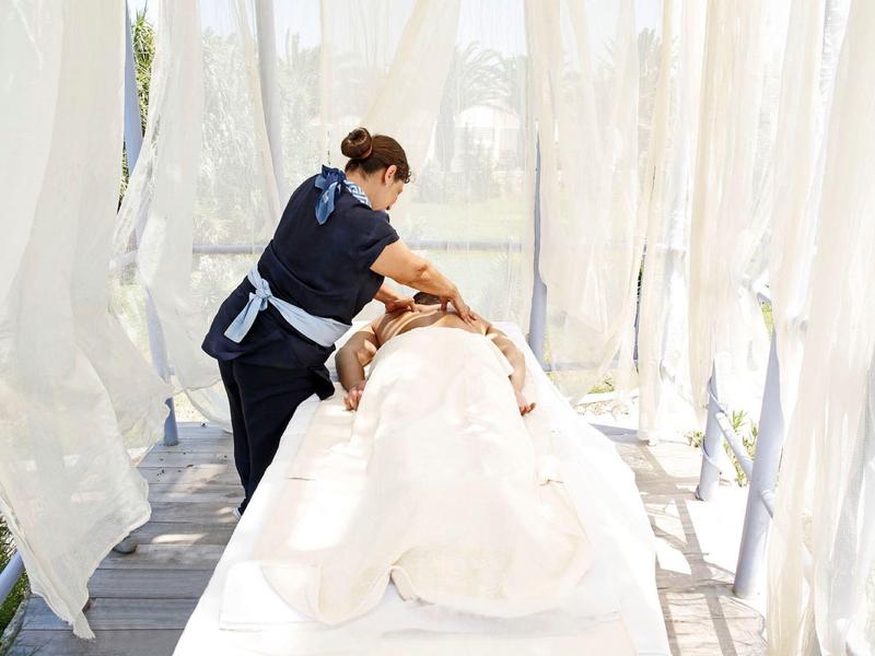 Masaż na zewnątrz na stole z białymi zasłonami i światłem naturalnym.