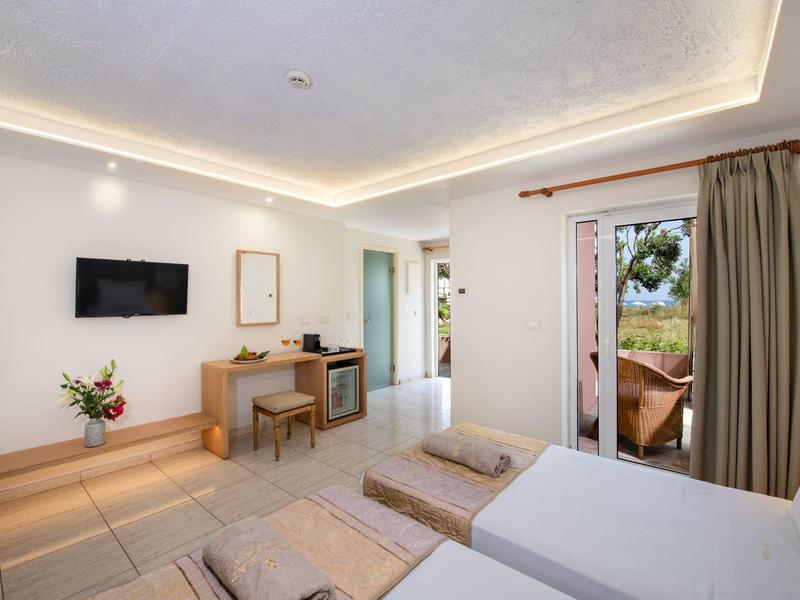 Jasny pokój hotelowy z dwoma łóżkami pojedynczymi, biurkiem, telewizorem i dostępem do balkonu.