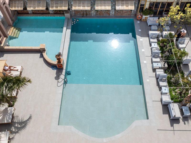 Trzy połączone baseny z leżakami i zielonymi roślinami na terenie hotelu.