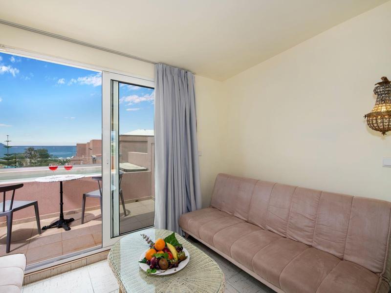 Jasny pokój z sofą, szklanym stolikiem i balkonem z widokiem na morze