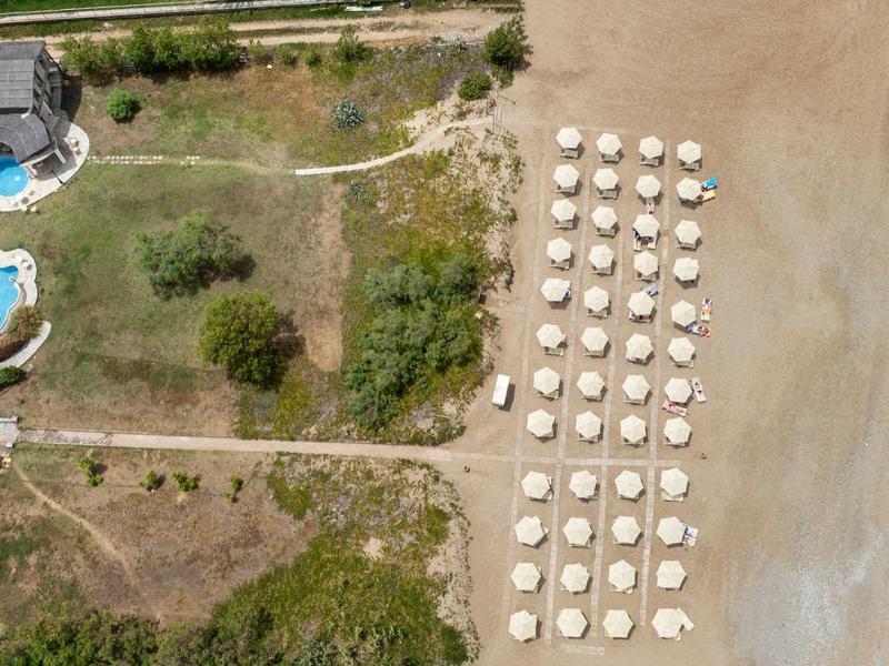 Widok z lotu ptaka na hotel z basenem, leżakami i parasolami na plaży.