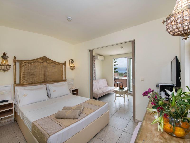 Jasny pokój hotelowy z dużym łóżkiem, przytulnym kącikiem wypoczynkowym i balkonem z widokiem na morze.