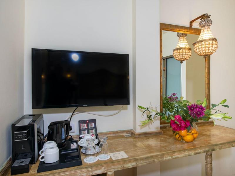 Nowoczesny serwis kawowy i telewizor w jasnym pokoju hotelowym z drewnianym stołem i kwiatową dekoracją.