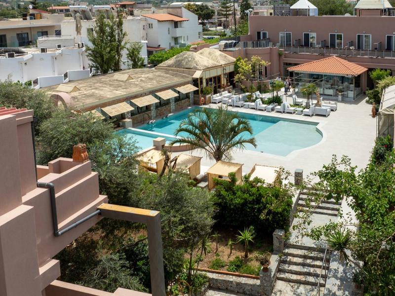 Widok na basen hotelowy z leżakami i okalającymi budynkami w słoneczny dzień