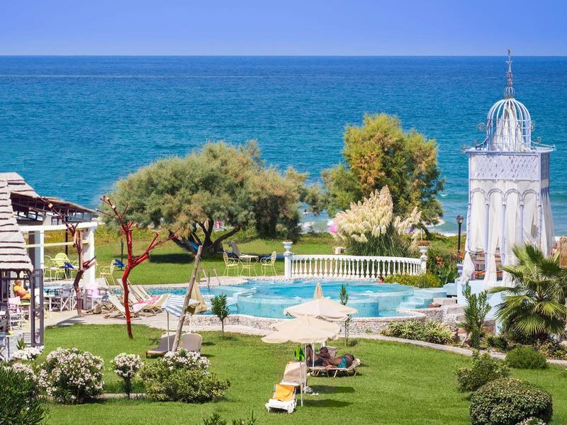 Ogród hotelowy z basenem, leżakami, drzewami i morzem w tle