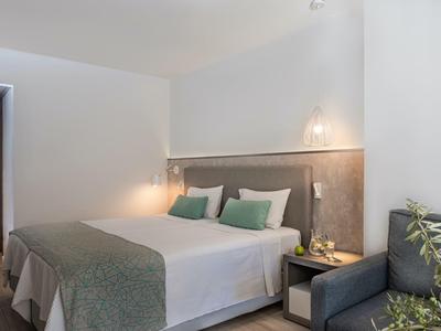 Modern hotel room with a large double bed, green accents, and a bedside table with lamp.