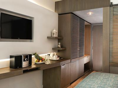Hotel room with wall-mounted TV, wooden shelves, coffee setup, and partial view of bed and closet.