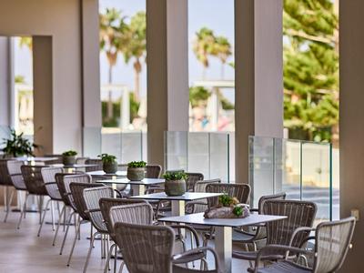 Outdoor hotel terrace with tables, chairs, and small potted plants, overlooking palm trees.