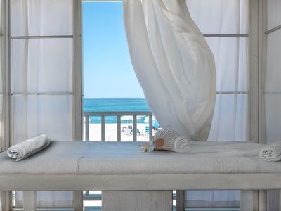 Massage table with white towels near a balcony overlooking the ocean with a flowing white curtain.