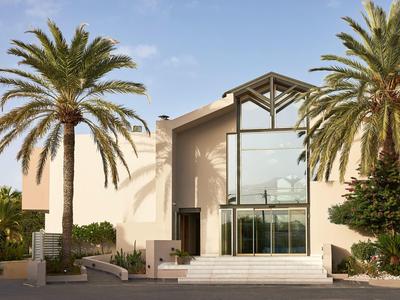 A modern hotel entrance framed by two tall palm trees under a clear blue sky.