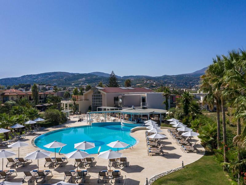 Outdoor pool with lounge chairs and umbrellas under clear blue sky near hotel.