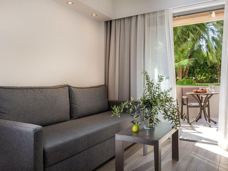 Cozy living area with gray sofa, small table, and balcony door overlooking greenery.
