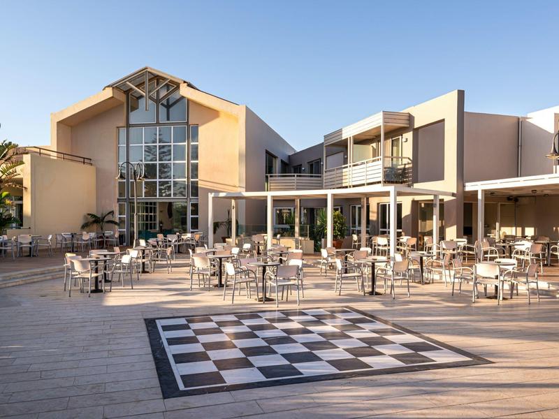 Outdoor seating area with tables and chairs at a modern hotel with large windows.