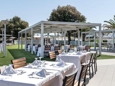 Outdoor hotel dining area with white tablecloths and modern pergolas under a clear sky.