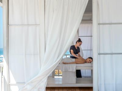 Massage therapist giving a massage to a person inside a white cabana by the sea.