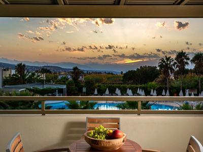 A balcony dining table set for two with a sunset view over a pool and palm trees.