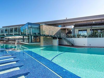 Outdoor hotel pool with sun loungers and modern glass architecture under blue sky.