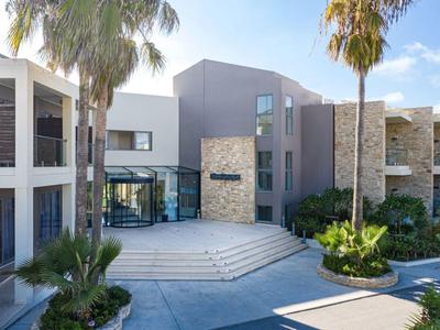 Modern hotel entrance with stone accents, palm trees, and spacious steps under a blue sky.