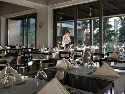 Elegant hotel restaurant with table settings and a server preparing a table near large windows.