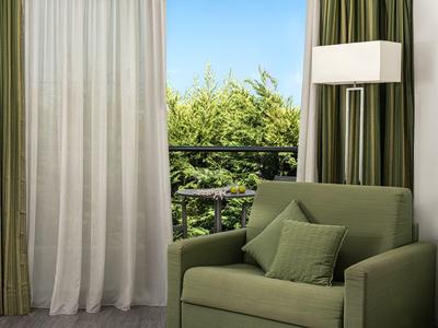Green armchair with cushions beside window with curtains and outdoor greenery view