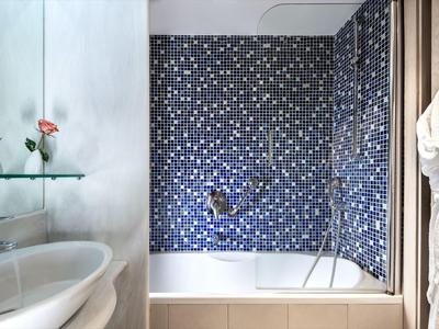 Bathroom with white sink, shelf with flowers, and bathtub with blue mosaic tiles.
