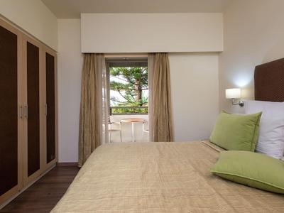 Hotel room with a large bed, green pillows, wardrobe, and a window with outdoor seating.