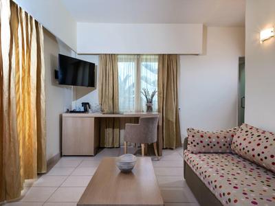 Cozy hotel room with polka-dot sofa, wooden table, desk, chair, and wall-mounted TV.