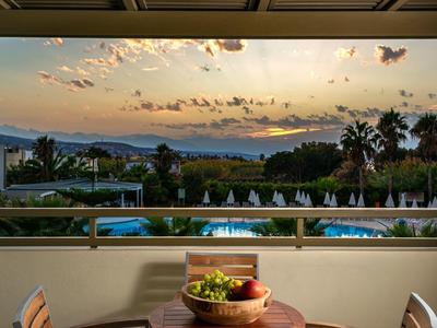 Sunset view over pool, palm trees, and dining table with fruit bowl at a resort.
