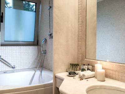 Modern bathroom with bathtub, shower, frosted window, sink, mirror, and toiletries.