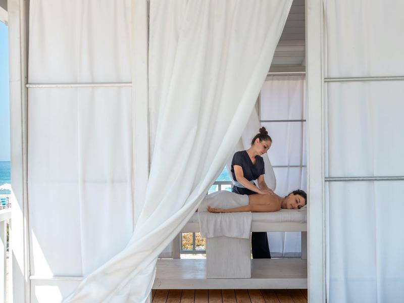 Massage therapist giving a massage to a person inside a white cabana by the sea.