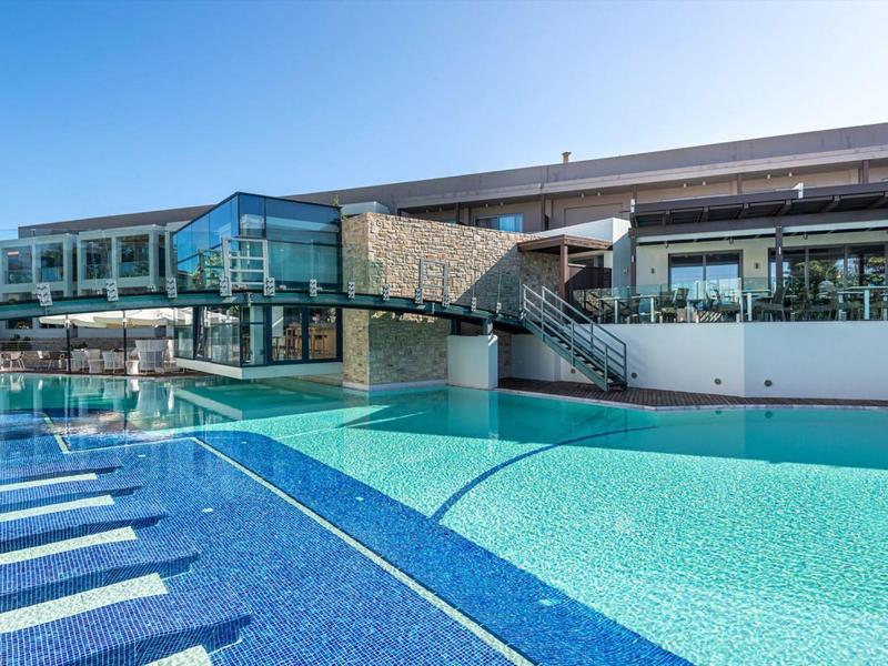 Outdoor hotel pool with sun loungers and modern glass architecture under blue sky.