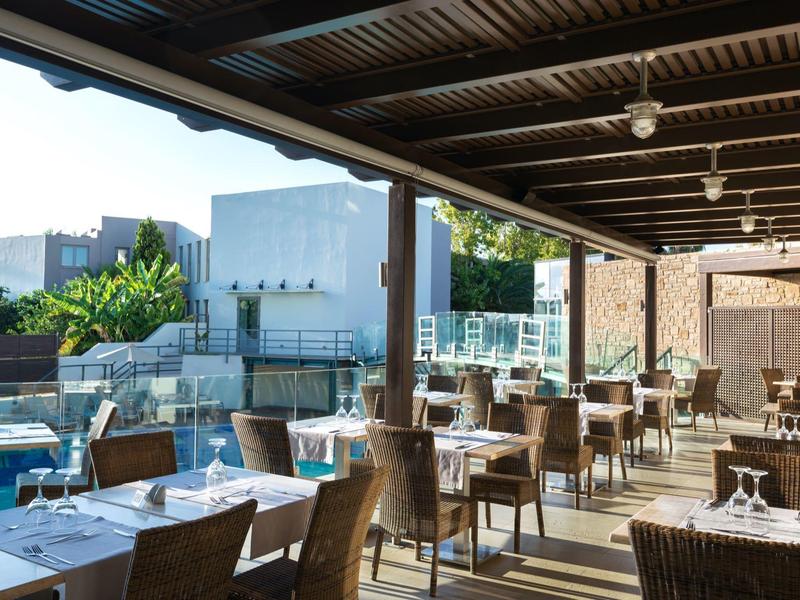 Spacious outdoor hotel dining area with wooden tables and chairs under a covered roof.