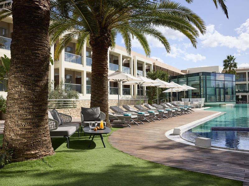 Outdoor pool area with lounge chairs and umbrellas at a modern hotel surrounded by palm trees.