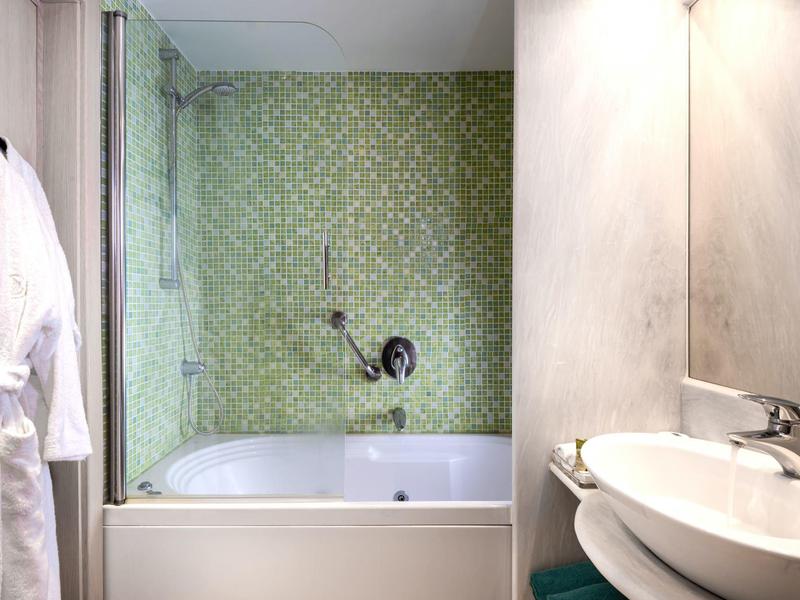Bathroom with white bathtub, glass shower door, green patterned wall, and white sink with mirror.