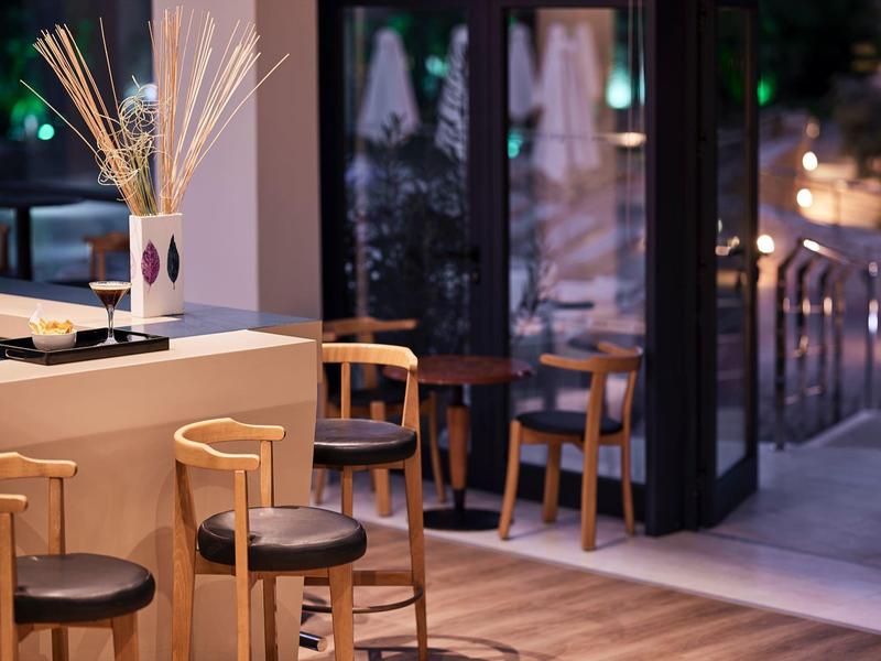 Cozy hotel bar area with wooden stools, soft lighting, and a plant arrangement on the counter.