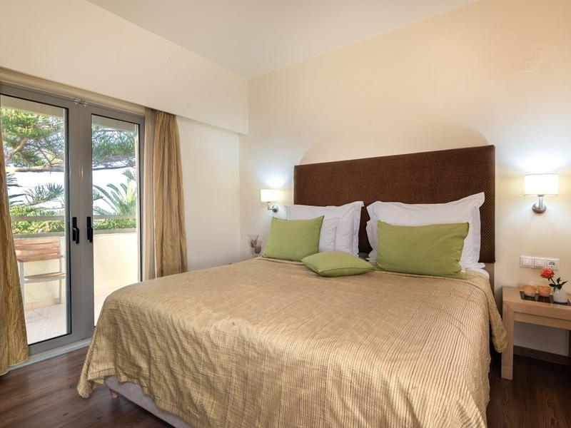 Cozy hotel room with a large bed, green pillows, nightstands, and a glass door to a balcony.