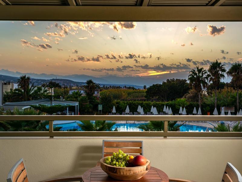 Sunset view over pool, palm trees, and dining table with fruit bowl at a resort.