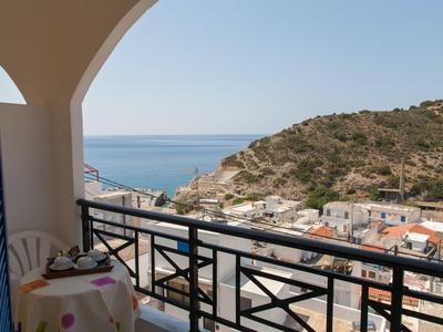 Balcone con tavolo, sedie e vista su colline e mare sotto un cielo sereno.