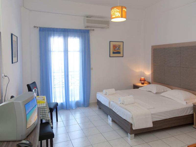 Jasny pokój hotelowy z podwójnym łóżkiem, telewizorem i balkonem z niebieskimi zasłonami.